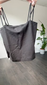 Juodas audinio trumpas viršus su plonais, reguliuojamais petnešomis, paprasto dizaino ir lygia tekstūra, pateiktas prieš patalpų augaliją.