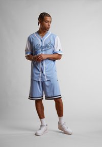 Maillot de sport bleu clair avec des manches blanches, portant "Starter" en écriture foncée. Associé à un short bleu clair avec des accents rayés noirs. Baskets blanches.