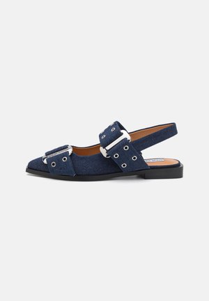 Zapato tipo slingback en denim azul oscuro con punta afilada, grandes hebillas plateadas y suela plana negra. Presenta ojales en las correas.
