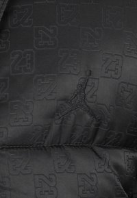 Sort puffer-materiale med et præget mønster af tallet "23" og et stikdelt Jumpman-logo, der skaber et tekstureret design.