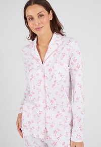 Ensemble de pyjama pour femmes en coton léger avec un fond blanc et un motif floral rose. Détails notables : col à revers et fermeture à boutons.