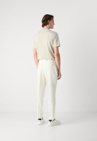 Beige lyhythihainen t-paita yhdistettynä kermaisiin housuihin, joissa on slim fit -leikkaus ja teksturoitu kangas, joita täydentävät valkoiset tennarit mustilla yksityiskohdilla.