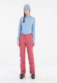 Light blue long-sleeve shirt and pink snow pants, featuring flat seams, belt loops, and textured knit beanie. Black ski boots complete the outfit.