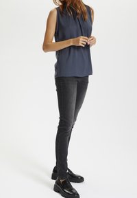 Hedvábný námořnický top bez rukávů s kulatým výstřihem, kombinovaný s tmavě šedými přiléhavými džíny a robustními černými polobotkami. Hladká textura a minimalistický design.
