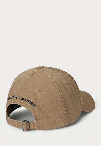 Kapa iz svetlo rjavega bombaža s krivim vizirjem. Ima izvezeno "RALPH LAUREN" v črni barvi na hrbtni strani ter nastavljiv pas s srebrno zaponko.