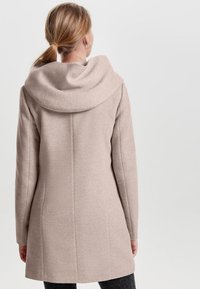 Light beige coat with a draped hood, tailored shape, and smooth texture, featuring seam details and a mid-length design.