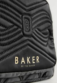 Borsa a tracolla nera trapuntata in raso con cuciture decorate, caratterizzata da un prominente logo "B" e dalla scritta dorata "BAKER by TED BAKER."