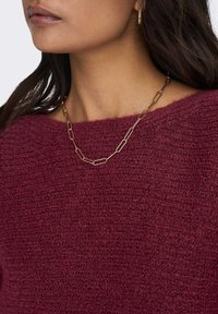 Bordeaux pletený svetr se širokým výstřihem, doplněný zlatým náhrdelníkem ze sponek do papíru, který dodává outfitu metalický akcent.