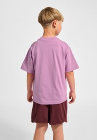 Kurzärmeliges T-Shirt mit Rundhalsausschnitt aus helllila Baumwolle, kombiniert mit bordeauxroten Shorts. Glatte Textur, lässige Passform und keine sichtbaren Muster.