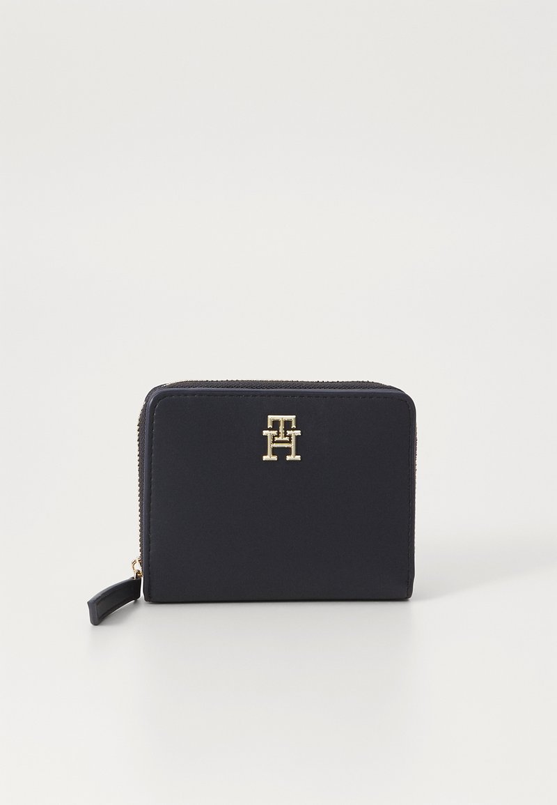 Portefeuille zippé bleu marine, fabriqué en matériau synthétique lisse, avec un logo doré sur le devant et une tirette de fermeture éclair texturée pour un accès facile.