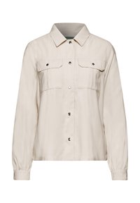 Vaaleanbeige nappipaita, jossa on kaulus, kaksi rintataskua, pitkät hihat joustavilla hihoilla ja sileä pinta. Metalliset nepparit.