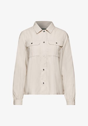 Beige overhemd met knopen en een kraag, twee borstzakken, lange mouwen met elastische manchetten en een gladde textuur. Metalen drukknopen.