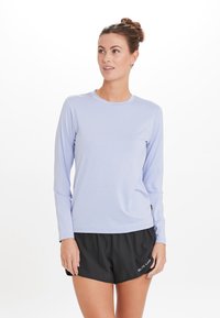 Lys lilla langærmet træningstop med rund halsudskæring, blød tekstur, båret sammen med sorte shorts med et logo på venstre side.
