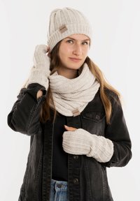 Roomwitte gebreide beanie, sjaal en vingerloze handschoenen met ribbelstructuur; gecombineerd met een zwarte spijkerjack en een nauwsluitend zwart top.