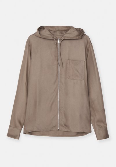 Φόρμα με κουκούλα σε ήσυχες καφέ αποχρώσεις, φτιαγμένη από μαλακό ύφασμα. Διαθέτει μπροστινές τσέπες και κουμπωτές μανσέτες για εφαρμοστό σχέδιο.