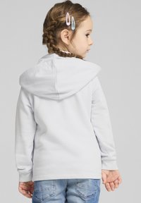 Hoodie grigio chiaro con una texture morbida, dotato di cappuccio con cordino, maniche lunghe e vestibilità comoda, abbinato a jeans denim blu.