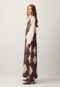 Dolga obleka v argyle vzorcu v bordo rdeči, kremni in sivi barvi. Izdelana iz teksturirane tkanine. Nosena čez kremno bluzo in kombinirana z rjavimi gležnjarji z visokimi petami.