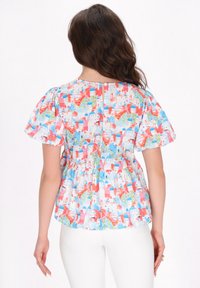 Farverig, let bluse med korte pufærmer og peplum-design. Viser et levende print af bygninger i blå, rød og grøn.