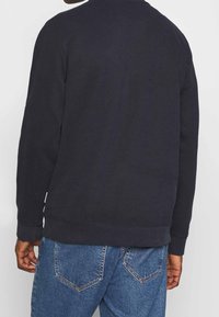 Granatowy dzianinowy sweter z miękkiego materiału, z okrągłym dekoltem i ściągaczami na rękawach. Widok z tyłu pokazuje prosty, gładki fason z luźnym krojem.