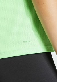 Světle zelené perforované sportovní tričko s embosovaným nápisem "AEROREADY" na spodním lemu; v kombinaci s černými hladkými legínami.