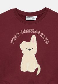 Μπορντό φούτερ από βαμβάκι με το κείμενο "ΚΛΑΜΠ ΚΑΛΥΤΕΡΩΝ ΦΙΛΩΝ" πάνω από μια εικονογράφηση ενός fluffy κρεμ σκύλου. Στρογγυλή λαιμόκοψη, χωρίς πρόσθετες λεπτομέρειες.