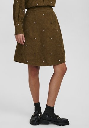 Falda marrón de pana con pequeñas flores blancas bordadas, llevada con calcetines negros y mocasines.