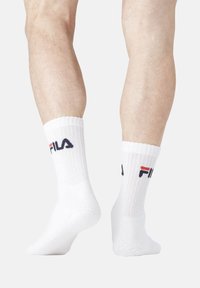 Chaussettes en coton blanc avec des bordures côtelées et un logo "Fila" imprimé en bleu marine et rouge. Longueur cheville courte, avec une texture lisse.