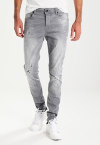 Grå denimjeans med slim fit, med färgfläckar och en urtvättad textur. Kombineras med vita sneakers.