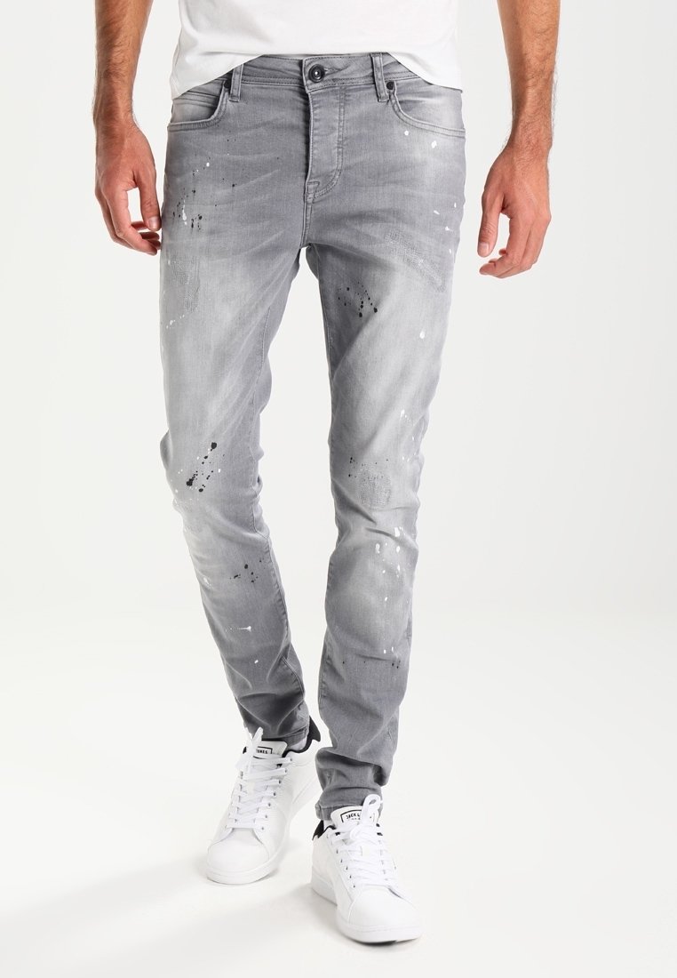 Grå denimjeans med slim fit, med färgfläckar och en urtvättad textur. Kombineras med vita sneakers.