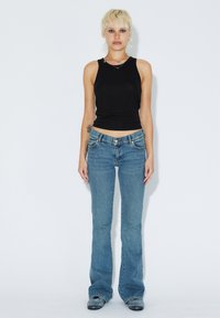 Černý top bez rukávů a světlé modré zvonové džíny. Materiál je hladký bavlněný; džíny mají klasický design s pěti kapsami a decentním prošíváním.