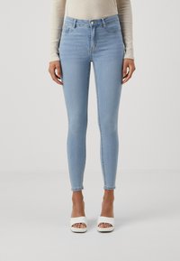 Jeans skinny de cintura alta em azul claro, com uma textura suave e ligeiramente desbotada. Apresenta bolsos frontais, um botão e um fecho com zíper.