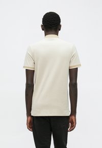 Beige kortermet polo skjorte med slim fit, med kontrasterende kant på kragen og ermene. Glatt tekstur og rene linjer.