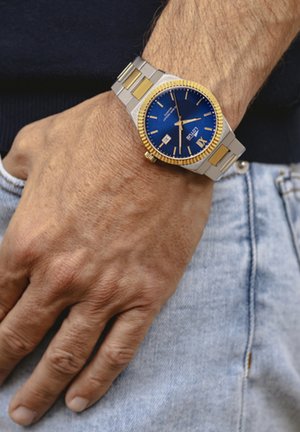 Montre en argent et doré avec un cadran bleu, bracelet en acier inoxydable et affichage de la date. Présente une lunette texturée et un design à maillons multiples.