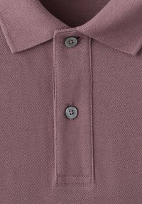 Gros plan sur le col d'un polo mauve avec deux boutons gris et un tissu en maille texturée.