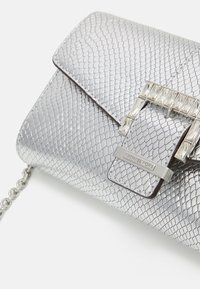 Hopeinen käärmeennahkatekstuuriin kyllästyneenä clutch, jossa on taitto-osa, metalliklipsi ja ketjun olkahihna. Klipsissä on kirkkaat, suorakulmaiset koristeet.