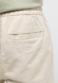 Pantalon beige décontracté avec taille élastique et une poche arrière présentant une discrète broderie MOSCONE.