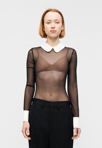 Διάφανο μαύρο μπλουζάκι με μακριά μανίκια και λευκή γιακά, με λεία υφή, συνδυασμένο με μαύρο ψηλόμεσο παντελόνι με λευκές μανσέτες.