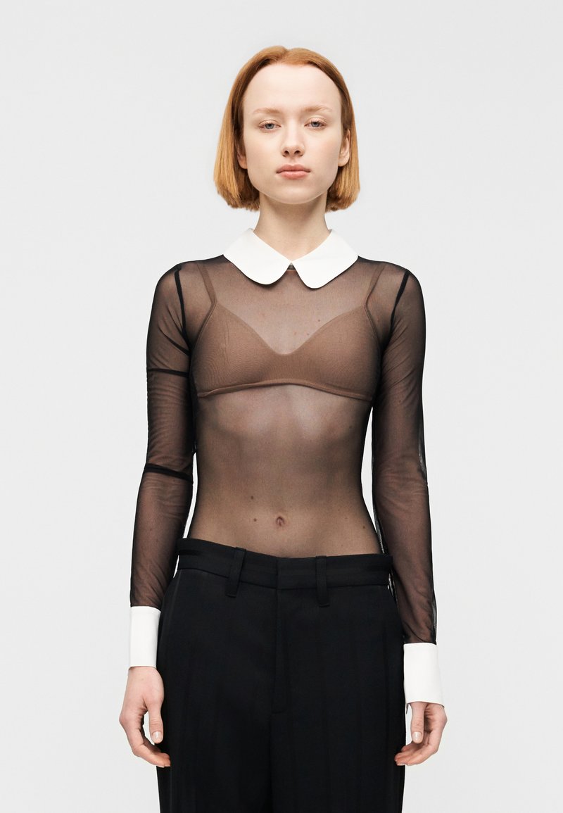 Διάφανο μαύρο μπλουζάκι με μακριά μανίκια και λευκή γιακά, με λεία υφή, συνδυασμένο με μαύρο ψηλόμεσο παντελόνι με λευκές μανσέτες.