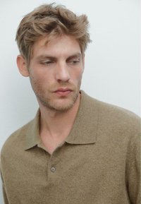 Beige gestricktes Poloshirt mit einer weichen Textur, ausgestattet mit einem klassischen Kragen und einer Knopfleiste mit zwei Knöpfen. Dezente Steppdetails am Kragen.