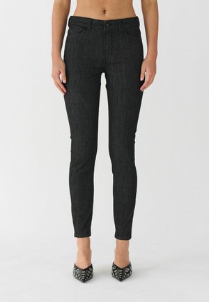 Black skinny jeans with a textured finish, a button closure, and front pockets. Paired with pointed black heels featuring silver accents.