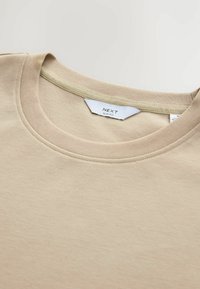 Beige slim fit t-shirt med en blød tekstur, rund hals, og kontrasterende inderskål detalje. Trykt label angiver mærke og pasform.