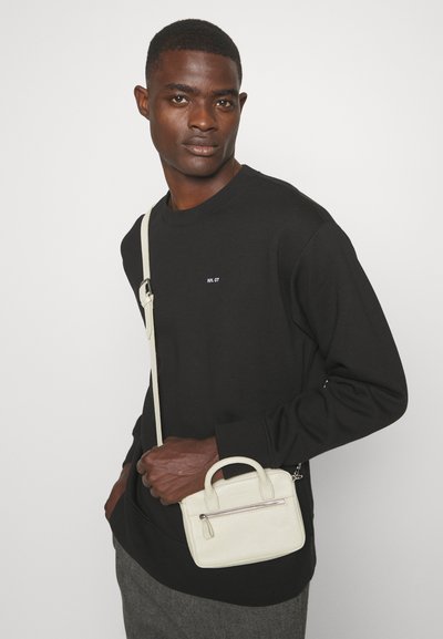 Zwarte sweatshirt met geborduurd logo, gecombineerd met een kleine crèmekleurige leren handtas met een rits en dubbele handgrepen.