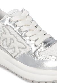 Sneaker bianche con accenti argentati, dotate di una tomaia in rete, linguetta imbottita e dettaglio del logo testurizzato. Suola spessa bianca con grip.