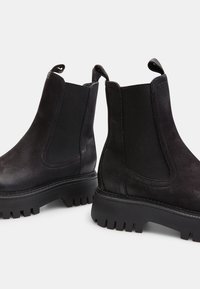 Botas Chelsea negras de cuero texturizado, con paneles laterales elásticos y una suela de goma gruesa con profundos surcos para mayor tracción.