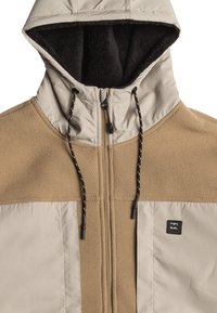 Veste à capuche beige et taupe en matériaux mélangés avec une finition texturée, dotée d'une fermeture éclair à l'avant, de cordons de serrage réglables et d'un écusson logo.