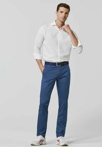 Witte linnen overhemd, blauwe broek, een gebloemde riem en witte sneakers met rode accenten, gepresenteerd in een staande pose tegen een neutrale achtergrond.
