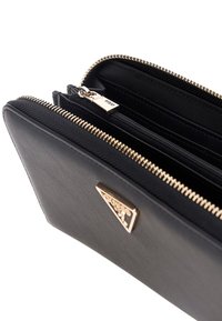 Portefeuille en cuir noir avec zips et quincaillerie de couleur dorée, comportant plusieurs compartiments et des détails de couture texturée.
