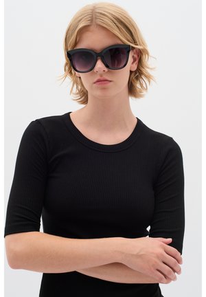 Black cat-eye sunglasses with dark lenses, thick plastic frame, and smooth texture, paired with a black ribbed short-sleeve top.