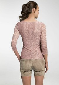 Spitzentop in sanftem Pink mit Dreiviertelärmeln, floralem Muster und gewellten Kanten, kombiniert mit beigen Wildleder-Shorts.