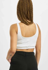 White cropped tank top with a ribbed texture, featuring a wide neckline and elastic hem. Paired with black pants.
